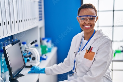 African american woman scientist smiling confident using computer at laboratory