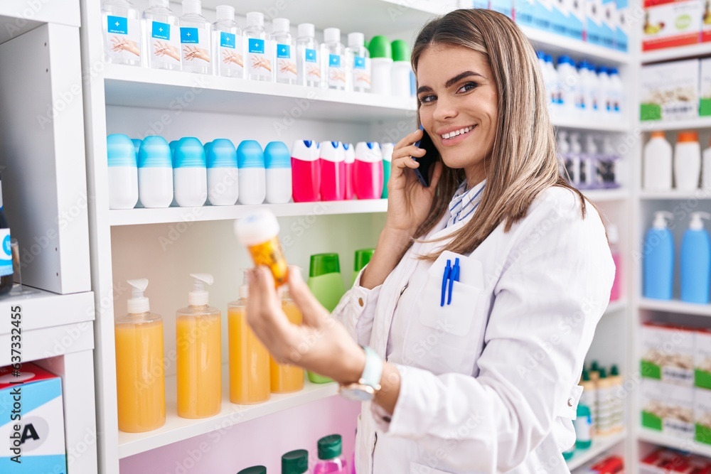 Young beautiful hispanic woman pharmacist holding pills bottle talking on smartphone at pharmacy