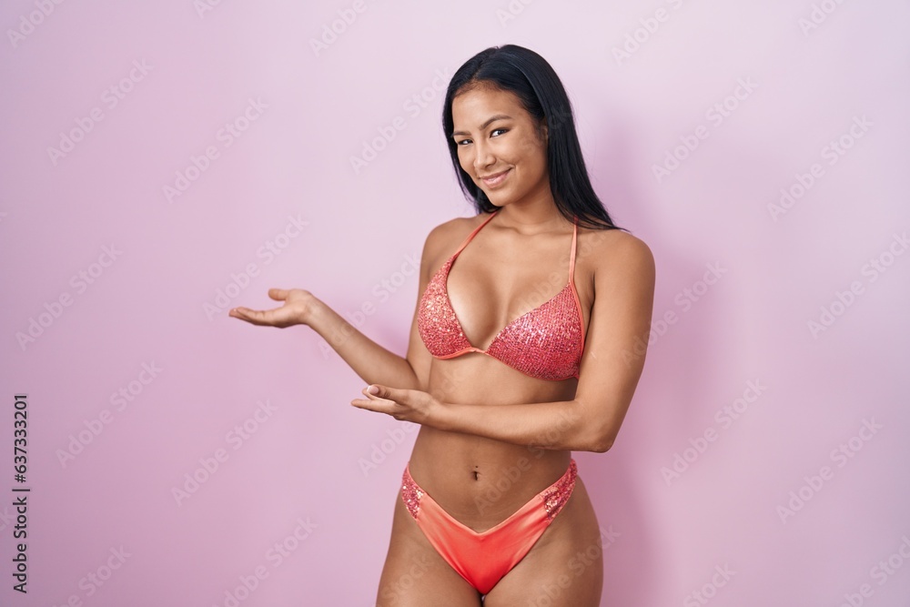 Hispanic woman wearing bikini inviting to enter smiling natural with open hand Hispanic woman wearing bikini inviting to enter smiling natural with open hand