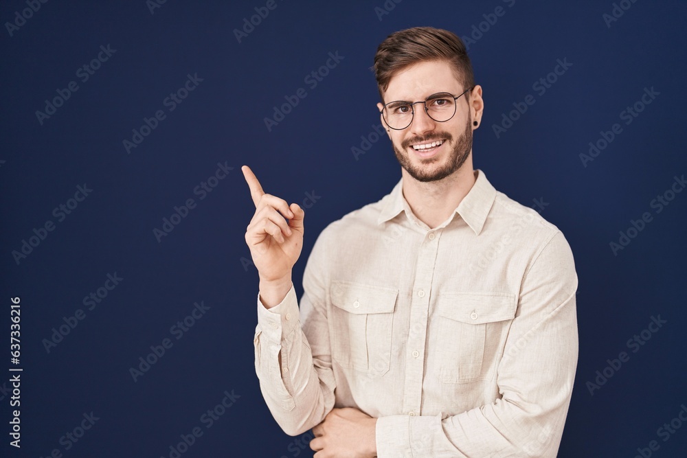 Hispanic man with beard standing over blue background with a big smile on face, pointing with hand and finger to the side looking at the camera. Hispanic man with beard standing over blue background with a big smile on face, pointing with hand and finger to the side looking at the camera.