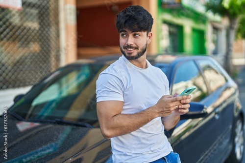 Young hispanic man using smartphone leaning on car at street