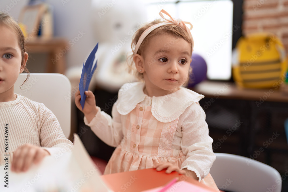 Two little girls drawing on notebook sitting on table at kindergarten Two little girls drawing on notebook sitting on table at kindergarten