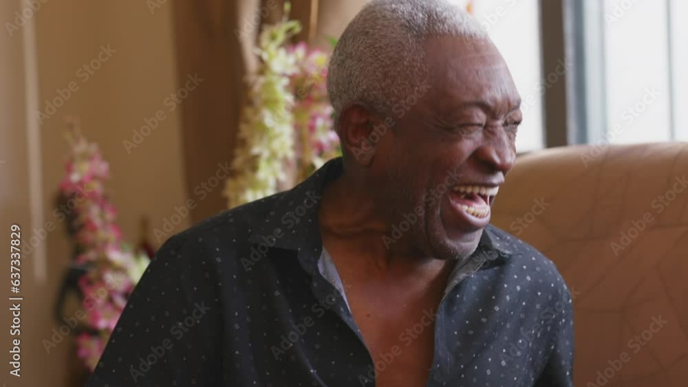 One joyful black senior man laughing and smiling sitting on couch, Candid authentic real life laughter of a happy African American older person One joyful black senior man laughing and smiling sitting on couch, Candid authentic real life laughter of a happy African American older person