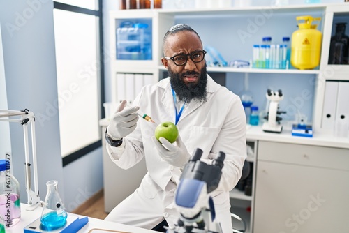 African american man working at scientist laboratory with apple clueless and confused expression. doubt concept.