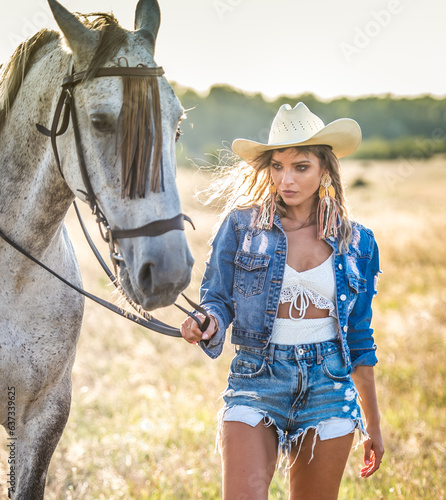 Obraz na płótnie Beautiful blonde woman with curly hair with white hat and horse. Portrait of a girl with denim and her horse. Beautiful girl interacting and having fun with a horse at the ranch w salonie