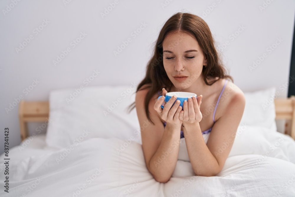 Young woman drinking cup of coffee sitting on bed at bedroom Young woman drinking cup of coffee sitting on bed at bedroom