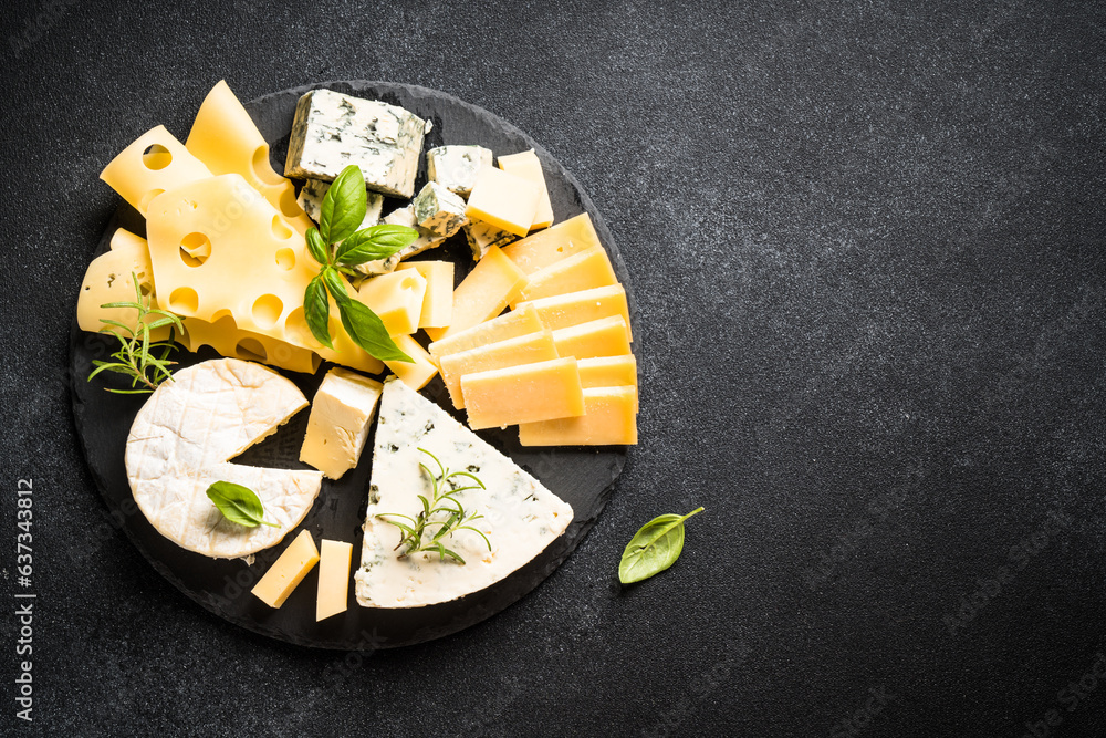 Cheese platter with craft cheese assortment on slate board at black background. Top view with copy space.