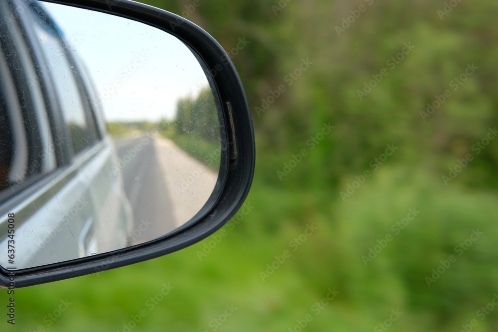 Side view mirror reflection of car auto in motion on road. Highway along green forest and trees in summer. Tourism and travel, journey trip concept. Beautiful nature and landscape. Car speeding road