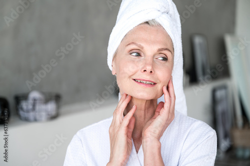 Woman with towel on head touching skin on cheek and neck