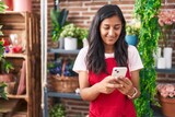 Young beautiful hispanic woman florist smiling confident using smartphone at flower shop