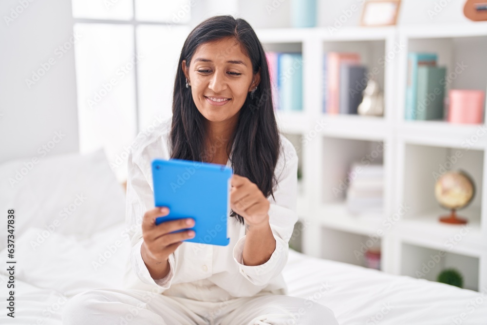 Young beautiful hispanic woman using touchpad sitting on bed at bedroom Young beautiful hispanic woman using touchpad sitting on bed at bedroom