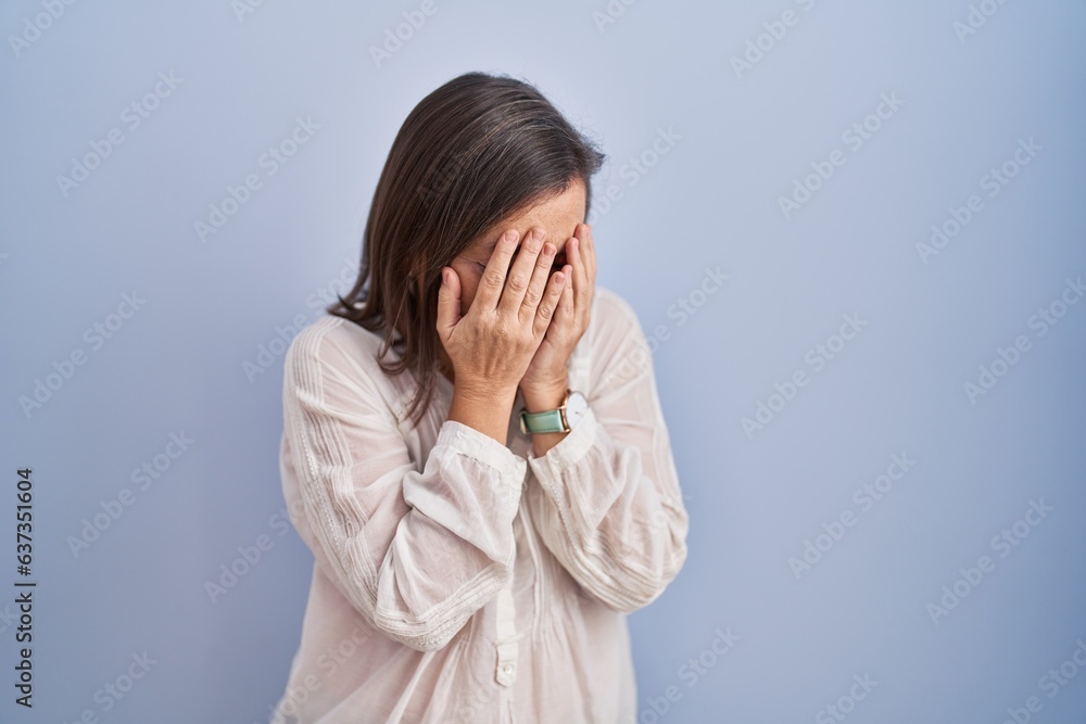 Middle age hispanic woman standing over blue background with sad expression covering face with hands while crying. depression concept. Middle age hispanic woman standing over blue background with sad expression covering face with hands while crying. depression concept.