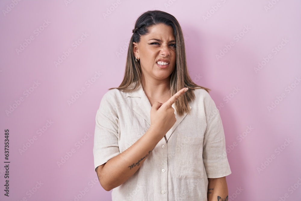 Fototapeta premium Blonde woman standing over pink background pointing aside worried and nervous with forefinger, concerned and surprised expression
