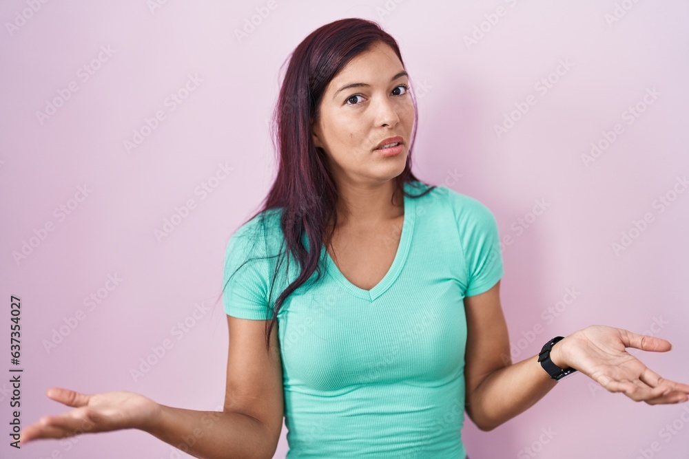 Young hispanic woman standing over pink background clueless and confused with open arms, no idea concept. Young hispanic woman standing over pink background clueless and confused with open arms, no idea concept.