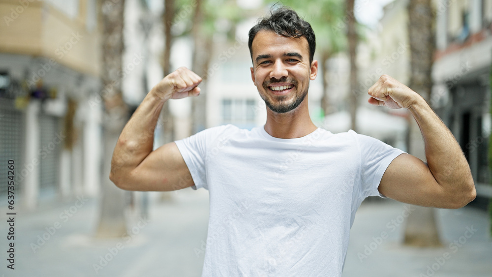 Fototapeta premium Young hispanic man smiling confident doing strong gesture with arms at street