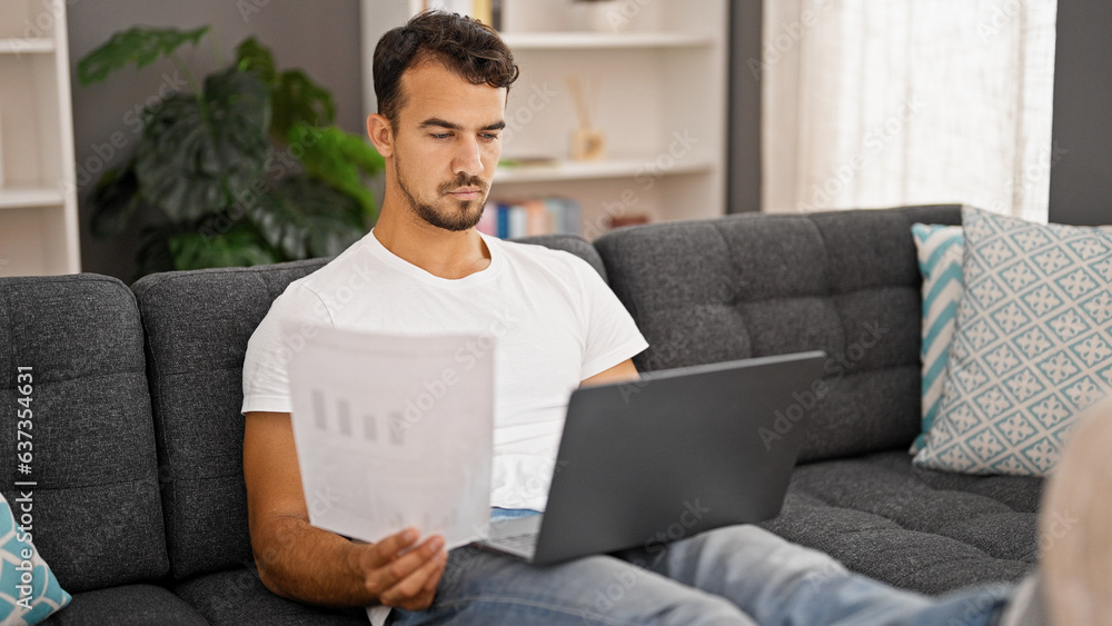 Young hispanic man using laptop reading paper at home Young hispanic man using laptop reading paper at home