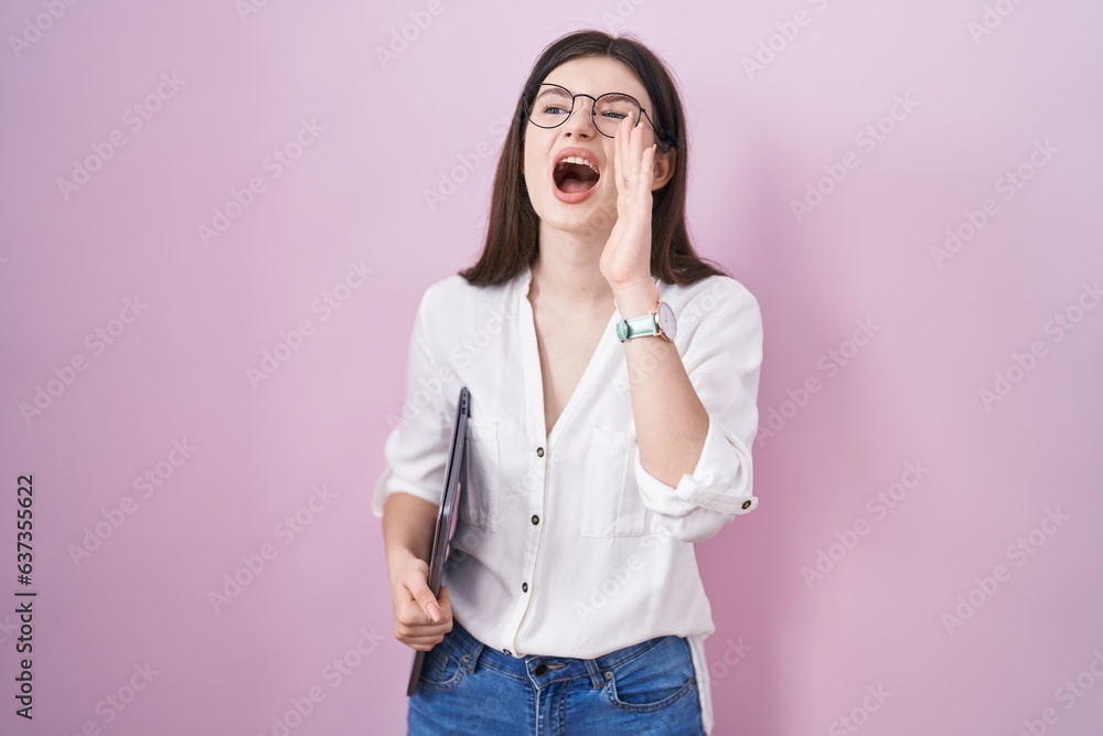 Young caucasian woman holding laptop shouting and screaming loud to side with hand on mouth. communication concept. Young caucasian woman holding laptop shouting and screaming loud to side with hand on mouth. communication concept.