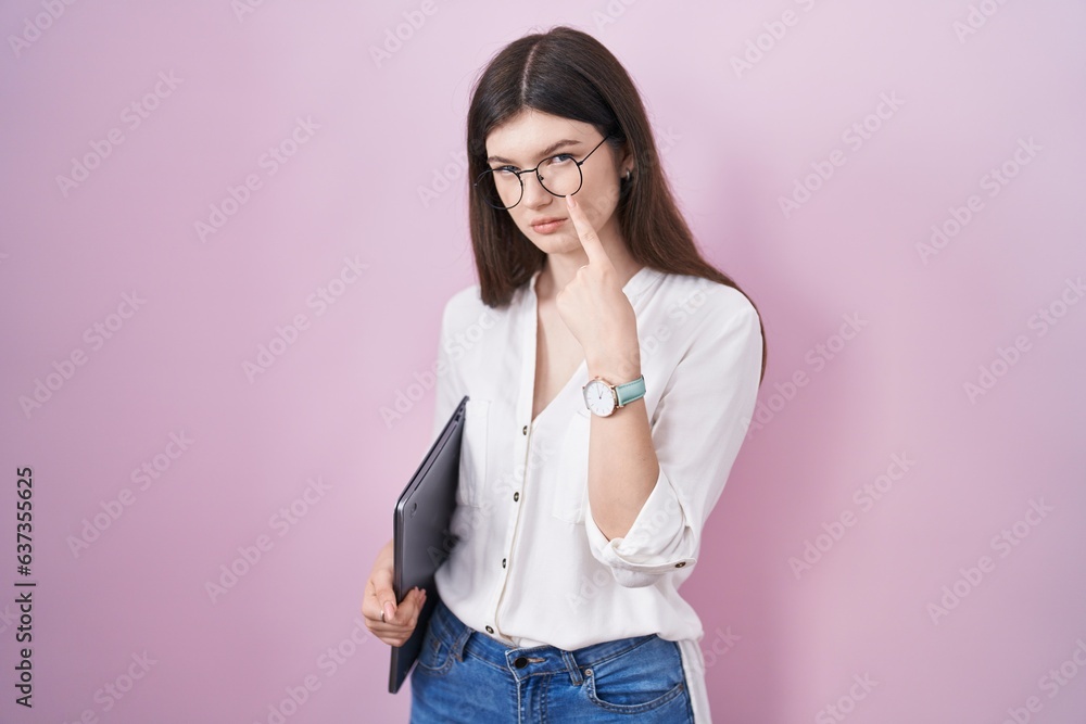 Young caucasian woman holding laptop pointing to the eye watching you gesture, suspicious expression Young caucasian woman holding laptop pointing to the eye watching you gesture, suspicious expression
