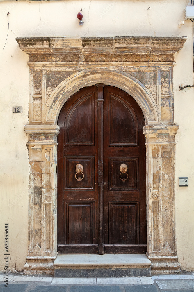 Old weather wooden door with stone arched lintel at an abandoned old mansion in Old Town of Rethymno, in Crete island, Greece, Europe. Old weather wooden door with stone arched lintel at an abandoned old mansion in Old Town of Rethymno, in Crete island, Greece, Europe.