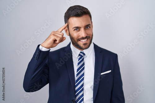 Handsome hispanic man wearing suit and tie smiling pointing to head with one finger, great idea or thought, good memory