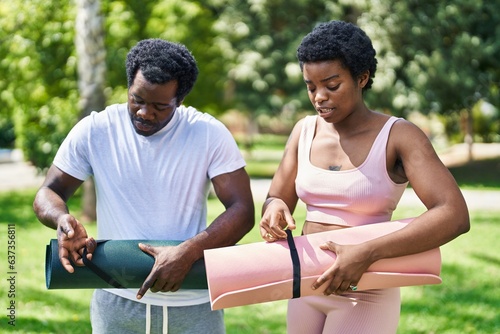 African american man and woman couple holding yoga mat with relaxed expression at park