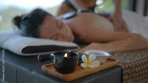 Close up of aroma lamp at the massage table with girl lying on it, back massage with stones and hands, relaxation in health spa resort, body care concept