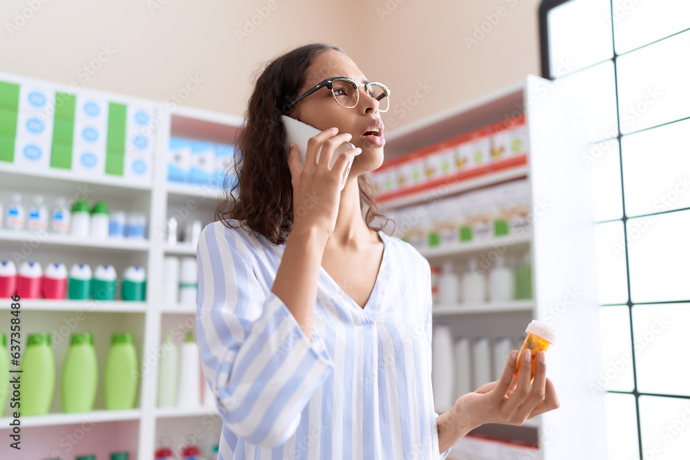Young african american woman customer talking on smartphone holding pills bottle at pharmacy