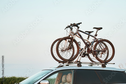 Mounted sport mountain bicycle silhouette on the car roof with evening sunlight rays background. Concept of safe items transportation using a car with roof rack