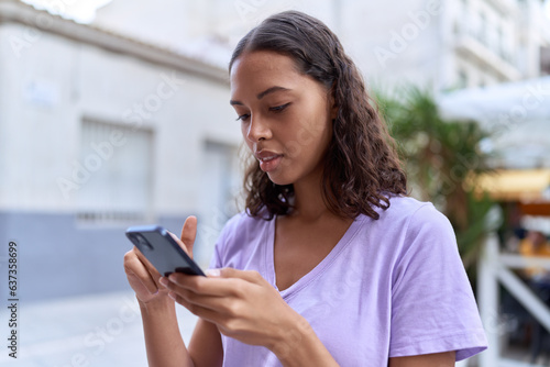 Young african american woman using smartphone with serious expression at street