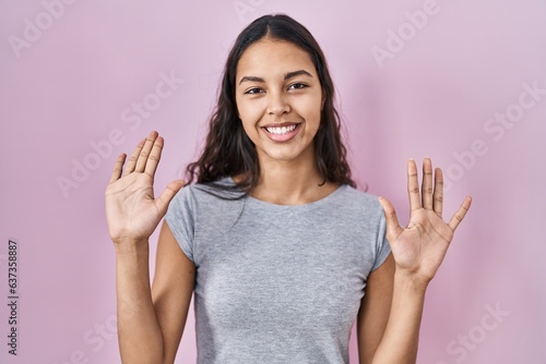 Young brazilian woman wearing casual t shirt over pink background showing and pointing up with fingers number ten while smiling confident and happy. © Krakenimages.com
