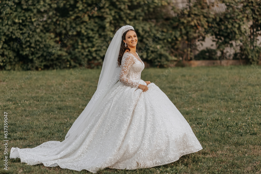 Portrait of the bride in a white dress and a crown on her head is walking in the park. Professional wedding makeup and hair. Beautiful young bride. Happy woman.