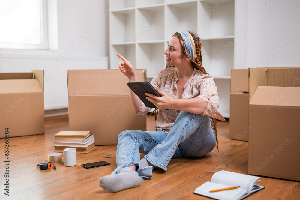 Modern ginger woman with braids using digital tablet while moving into new apartment. Modern ginger woman with braids using digital tablet while moving into new apartment.