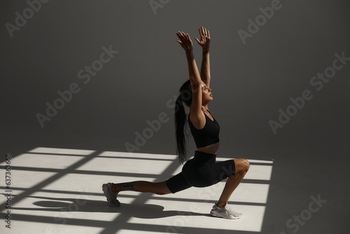 a tanned sports girl in a black suit is training in a yoga class in a fitness studio. white room. morning workout. warm-up