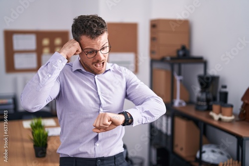 Young hispanic man at the office looking at the watch time worried, afraid of getting late