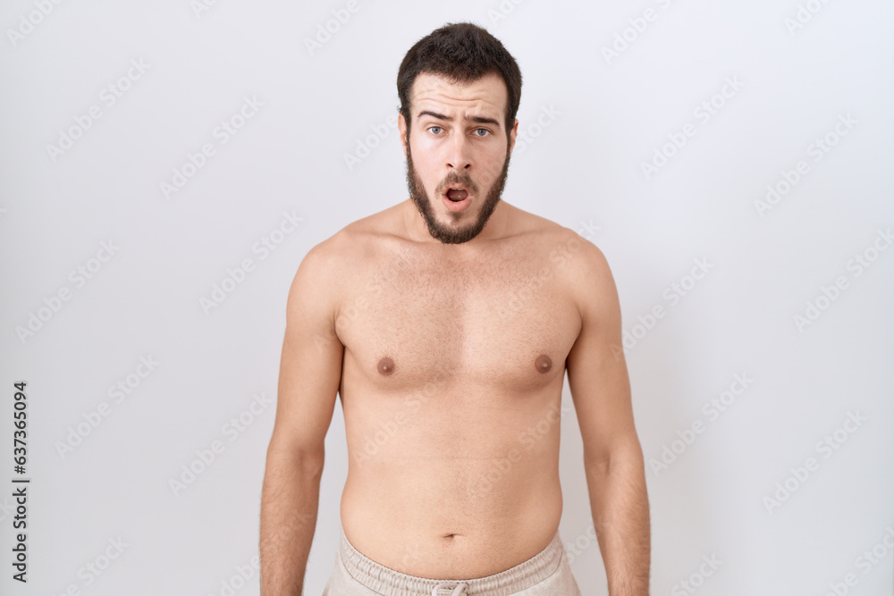 Young hispanic man standing shirtless over white background afraid and shocked with surprise expression, fear and excited face.
