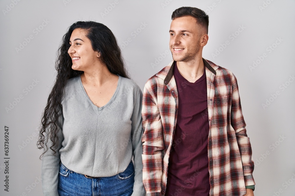 Young hispanic couple standing over white background looking away to side with smile on face, natural expression. laughing confident. Young hispanic couple standing over white background looking away to side with smile on face, natural expression. laughing confident.