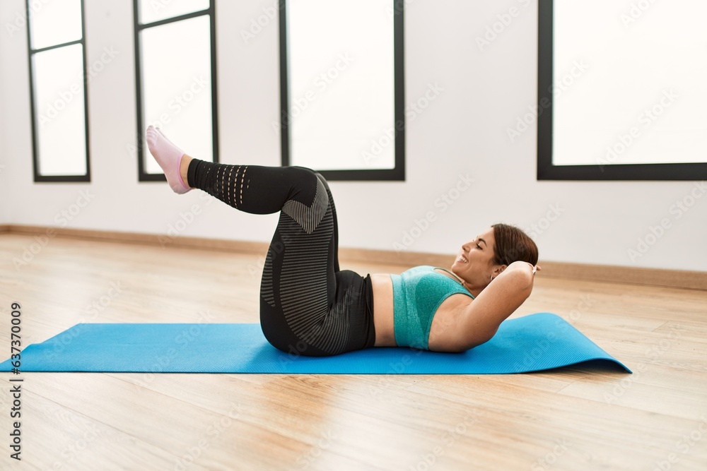Young beautiful hispanic woman training abs exercise at sport center
