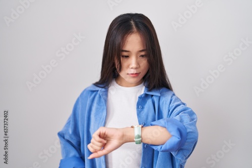 Young chinese woman standing over white background checking the time on wrist watch, relaxed and confident © Krakenimages.com