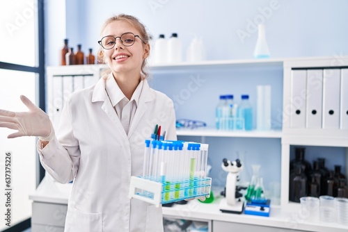 Young caucasian woman working at scientist laboratory holding samples celebrating achievement with happy smile and winner expression with raised hand