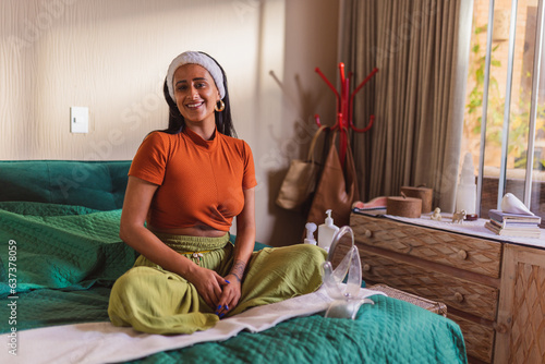 Jovem indigena, com faixa no cabelo, sentada na cama com um espelhinho para cuidar da pele. photo