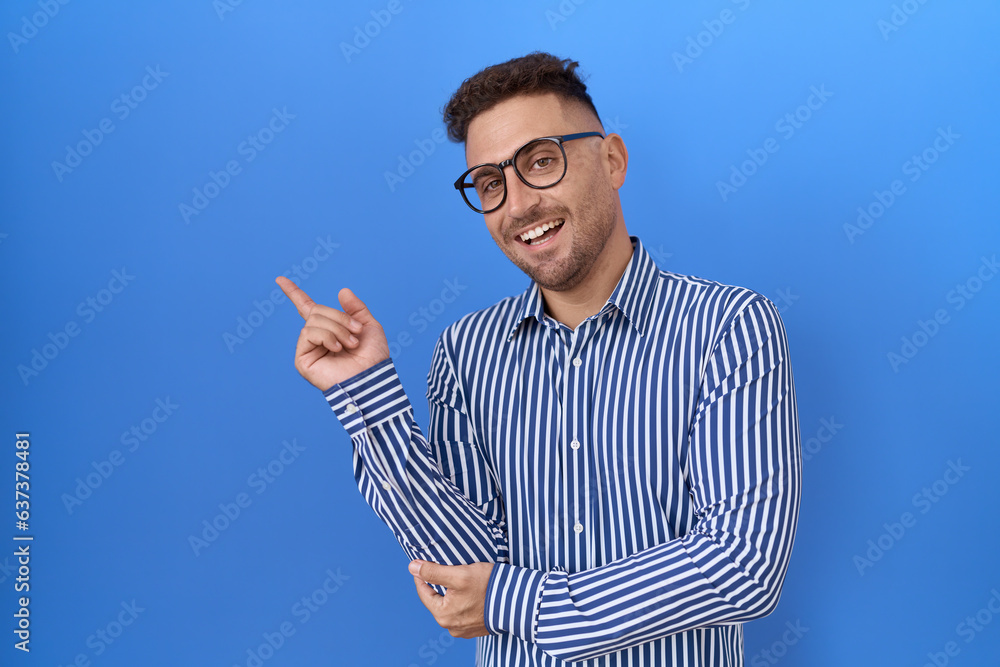Hispanic man with beard wearing glasses with a big smile on face, pointing with hand finger to the side looking at the camera. Hispanic man with beard wearing glasses with a big smile on face, pointing with hand finger to the side looking at the camera.