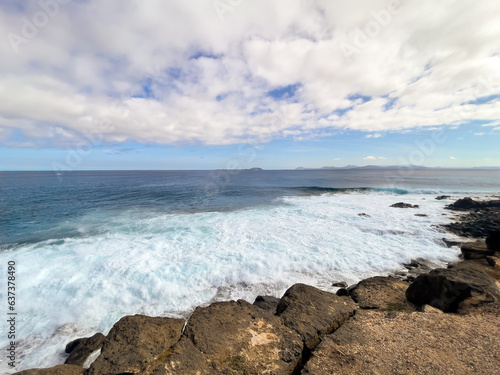 Ocean coast, sea surf, white foam from the wave, Fuerteventura is on the horizon
