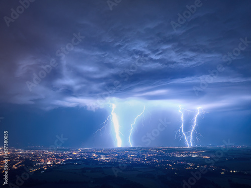 Spectacular, aerial shot of a city hit by multiple lightning. Dramatic, real drone shot of a massive storm over city. Lightning between the clouds and the ground. Blue and purple colors.
