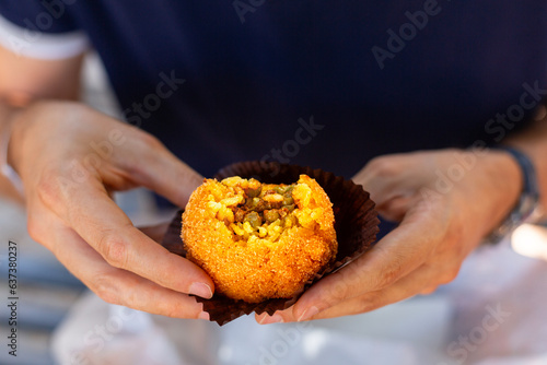 A man eating arancini, italian rice ball al ragu or al sugo, that is stuffed with meat, peas and tomato sauce and spices, coated with breadcrumbs and deep fried. Sicilian street food, cuisine.