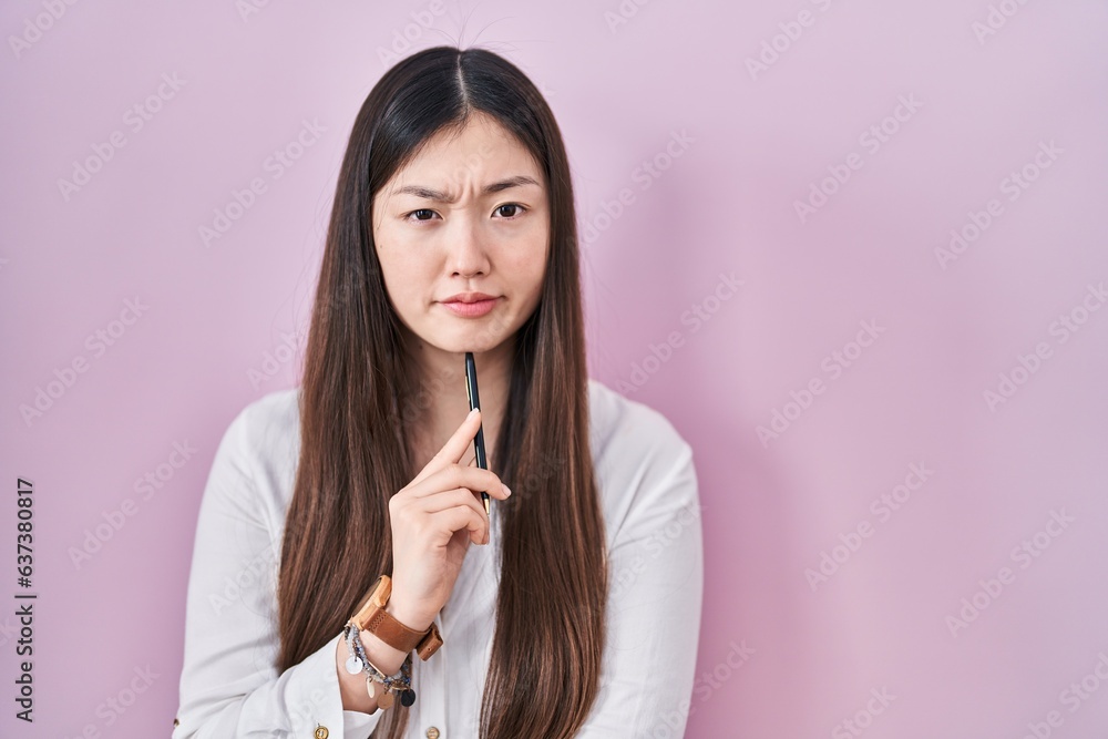Chinese young woman holding pencil over pink background skeptic and nervous, frowning upset because of problem. negative person. Chinese young woman holding pencil over pink background skeptic and nervous, frowning upset because of problem. negative person.