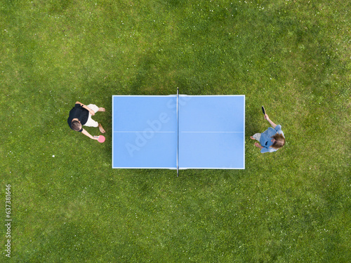 Aerial view people playing ping pong match outdoor. Top view two boys playing table tennis on a green grass lawn. Aerial view outdoor sport
