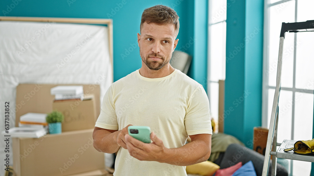 Obraz premium Young man using smartphone standing with serious face at new home