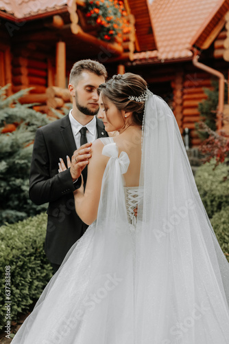 gorgeous elegant luxury bride with veil blowing in the wind and stylish groom kiss on the street near tall autumn trees and wooden houses