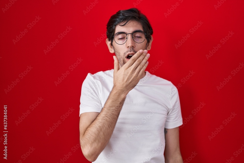 Young hispanic man standing over red background bored yawning tired covering mouth with hand. restless and sleepiness. Young hispanic man standing over red background bored yawning tired covering mouth with hand. restless and sleepiness.