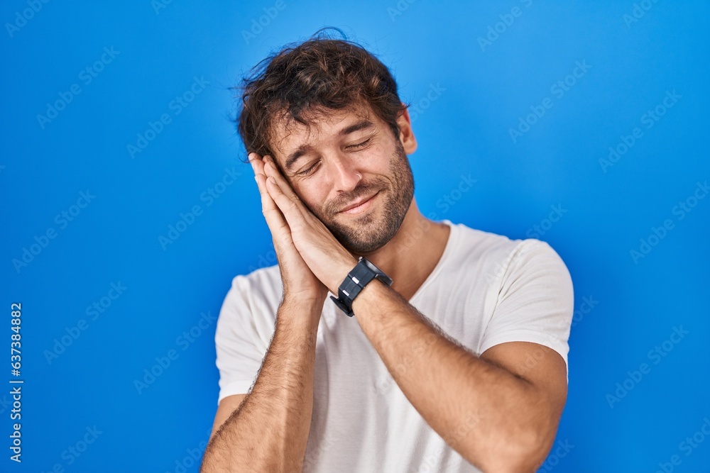 Hispanic young man standing over blue background sleeping tired dreaming and posing with hands together while smiling with closed eyes. Hispanic young man standing over blue background sleeping tired dreaming and posing with hands together while smiling with closed eyes.
